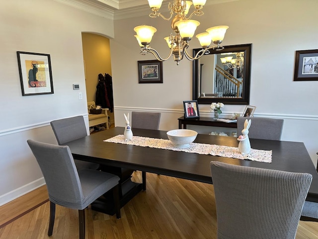 dining area with arched walkways, ornamental molding, wood finished floors, and a chandelier