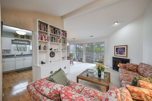living room with wood finished floors, visible vents, a lit fireplace, and lofted ceiling with beams