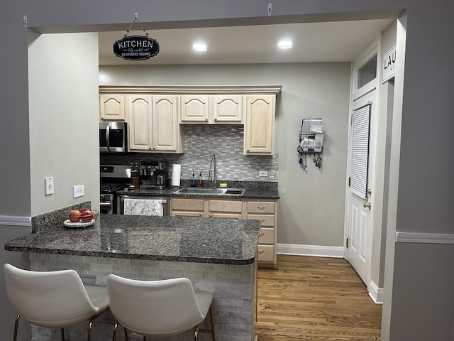 kitchen with appliances with stainless steel finishes, a sink, a peninsula, decorative backsplash, and light wood-type flooring