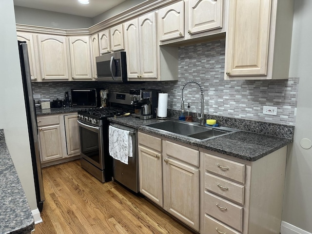 kitchen with dark countertops, tasteful backsplash, a sink, light wood finished floors, and stainless steel appliances