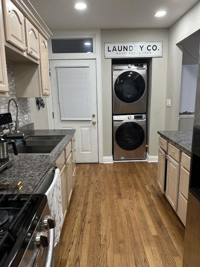 kitchen with a sink, dark wood finished floors, dark stone countertops, gas range, and stacked washer and clothes dryer