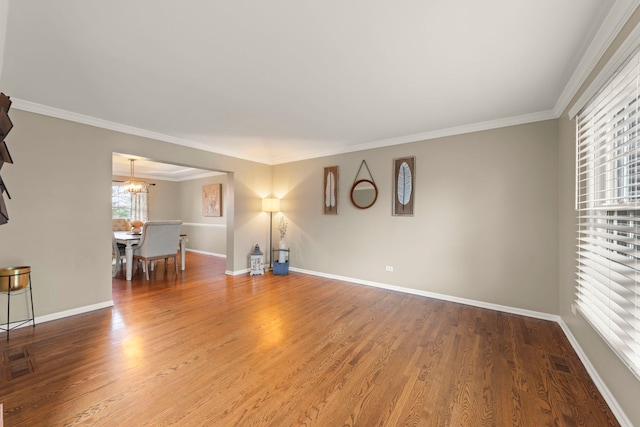 unfurnished living room featuring ornamental molding, wood finished floors, a chandelier, and baseboards