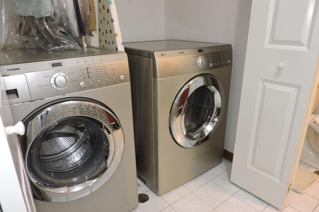 clothes washing area featuring laundry area, light tile patterned floors, and washer and clothes dryer