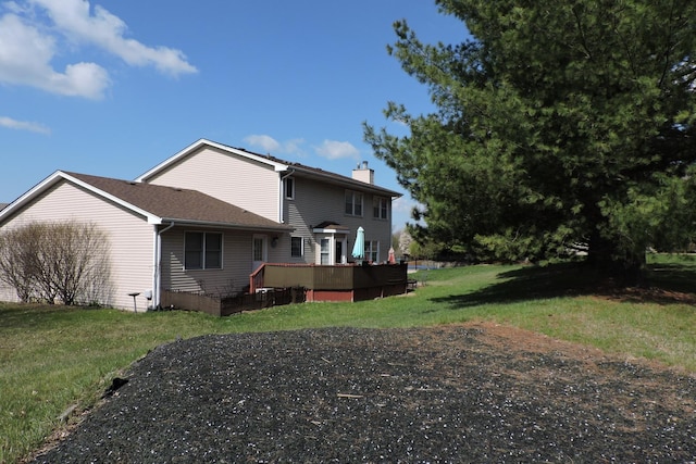 back of property with a chimney, a wooden deck, and a lawn