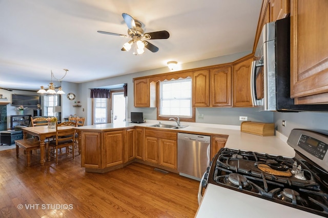 kitchen with a peninsula, a ceiling fan, brown cabinets, appliances with stainless steel finishes, and a sink