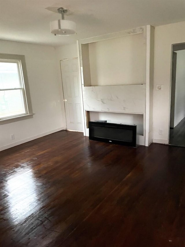 unfurnished living room with baseboards, a glass covered fireplace, and dark wood finished floors