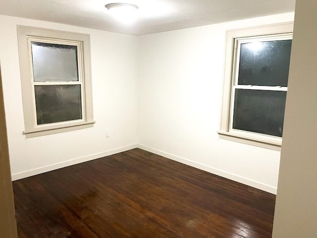 spare room with baseboards and dark wood-style floors