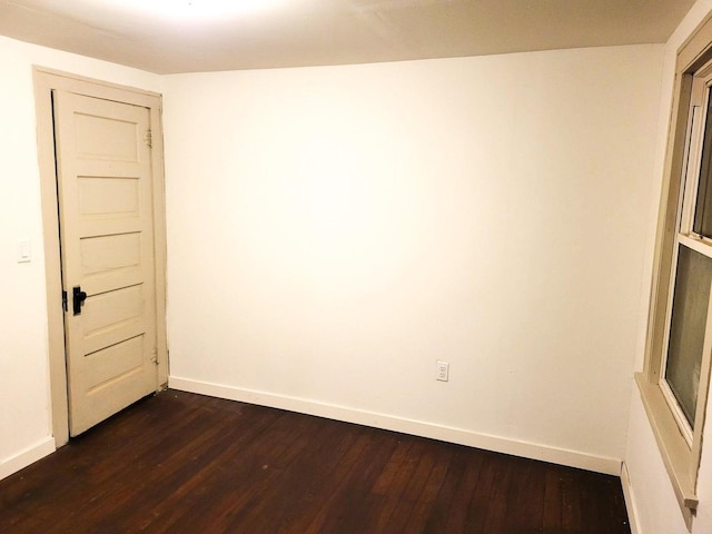 spare room featuring baseboards and dark wood-type flooring