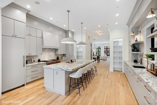 kitchen featuring a spacious island, paneled refrigerator, light wood-style floors, backsplash, and custom range hood