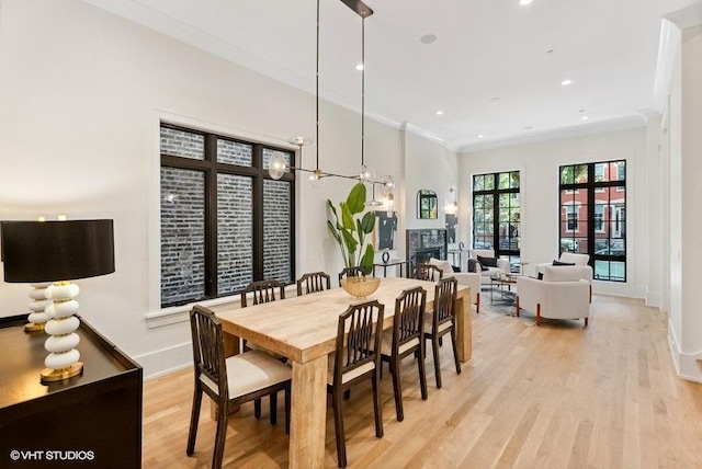 dining space with crown molding, light wood-style flooring, a fireplace, baseboards, and recessed lighting