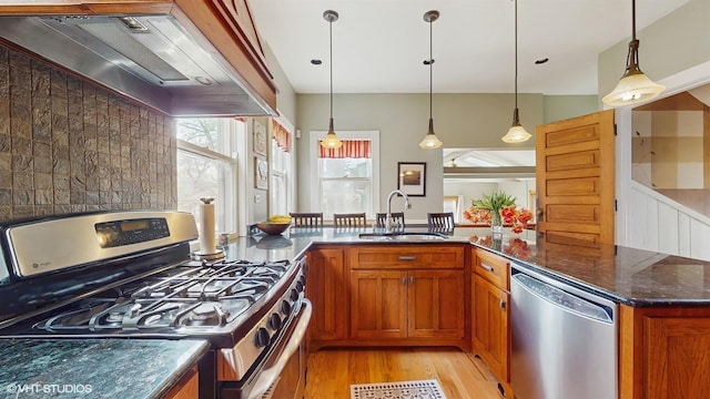 kitchen with brown cabinets, custom range hood, a sink, appliances with stainless steel finishes, and light wood finished floors