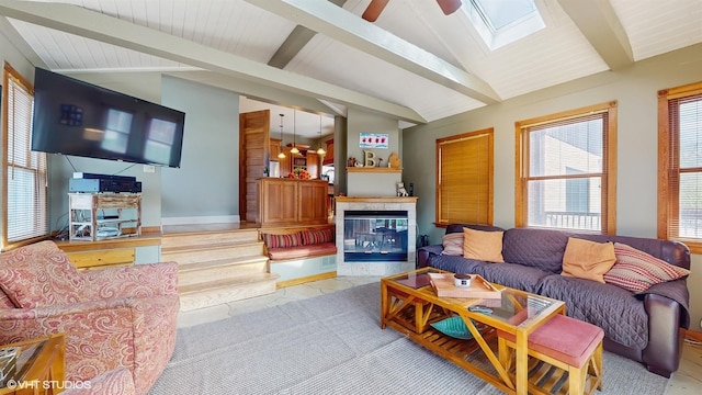 living room featuring baseboards, ceiling fan, and vaulted ceiling with skylight
