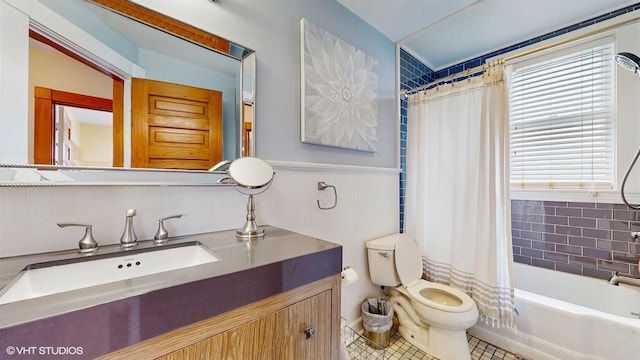 full bath featuring tile patterned floors, wainscoting, shower / bath combination with curtain, toilet, and vanity