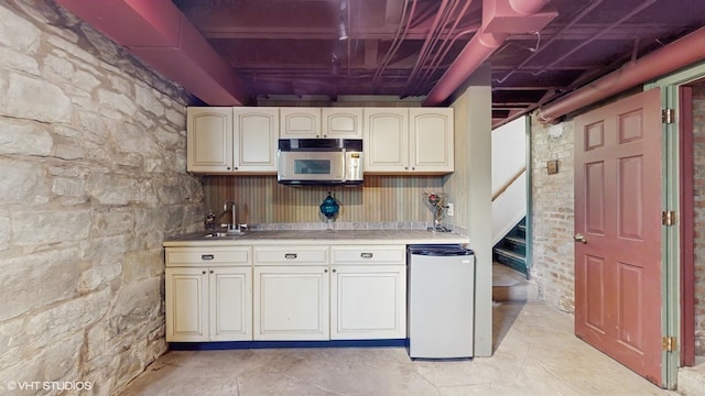 kitchen with stainless steel microwave, refrigerator, cream cabinets, and tile countertops
