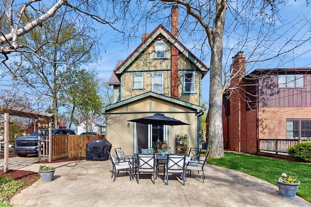 rear view of property featuring a patio, outdoor dining space, a chimney, and fence