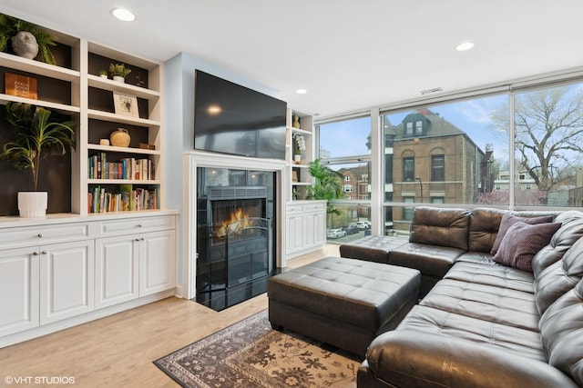 living area featuring recessed lighting, a tile fireplace, built in features, expansive windows, and light wood-style floors