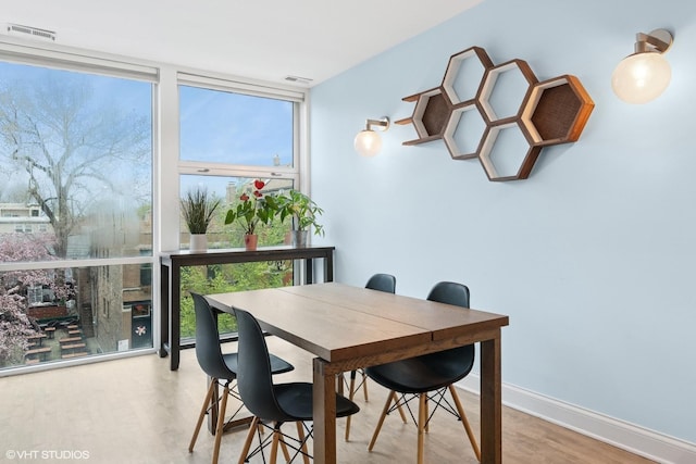 dining room with a wall of windows, visible vents, and wood finished floors