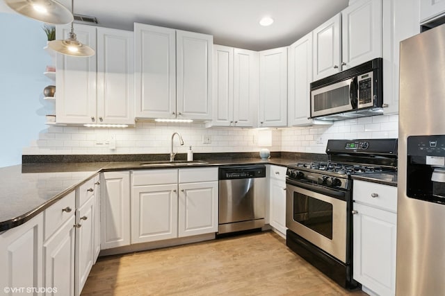 kitchen with dark countertops, white cabinets, appliances with stainless steel finishes, and a sink