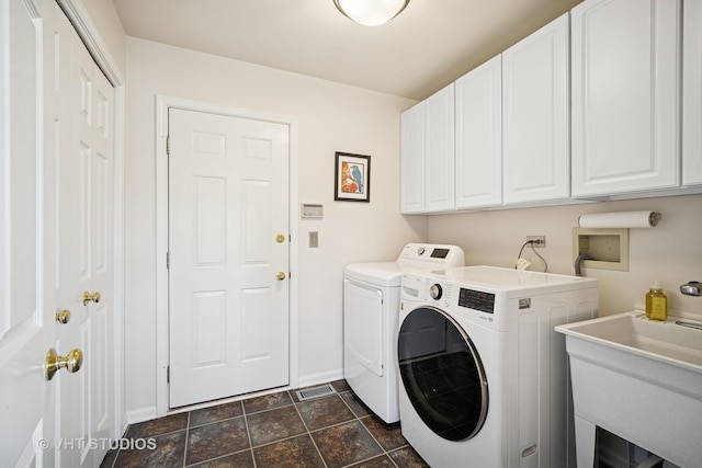washroom featuring stone finish floor, washing machine and clothes dryer, cabinet space, a sink, and baseboards