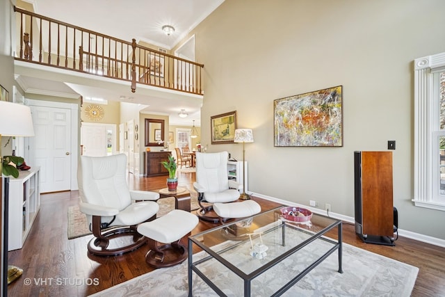 living room featuring crown molding, baseboards, a high ceiling, and wood finished floors