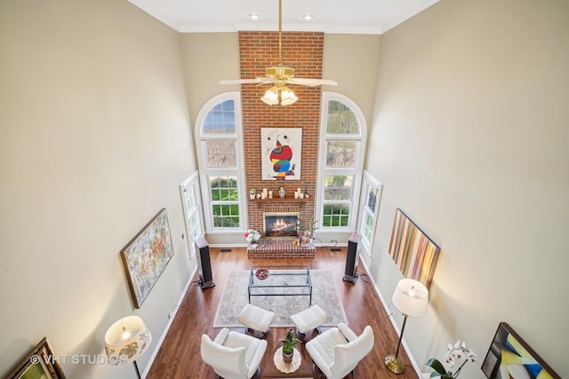 living room with a brick fireplace, a towering ceiling, wood finished floors, baseboards, and ceiling fan