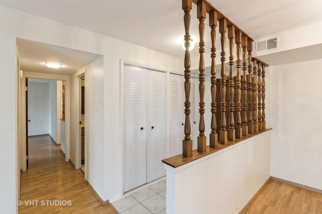 hallway featuring baseboards, light wood-type flooring, and visible vents