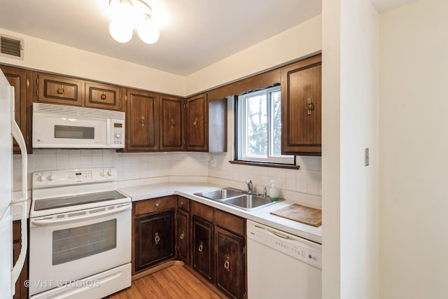 kitchen featuring white appliances, visible vents, a sink, backsplash, and light countertops