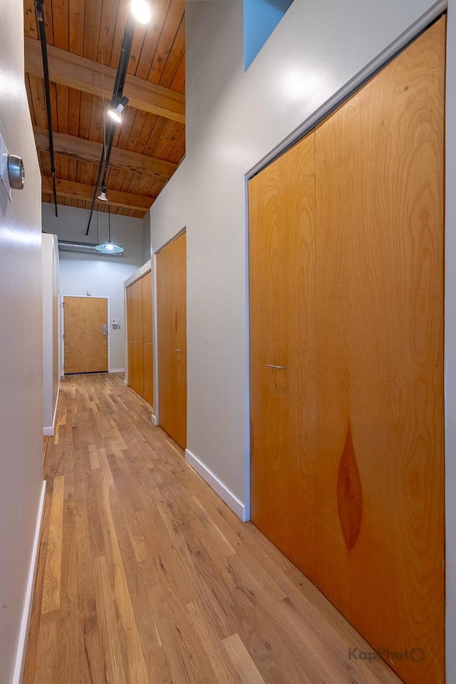 hall featuring baseboards, light wood-type flooring, wood ceiling, and lofted ceiling with beams
