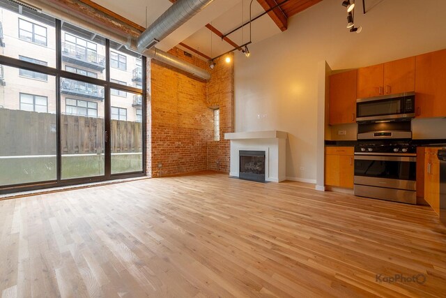 unfurnished living room with a fireplace, light wood-style flooring, a high ceiling, and brick wall