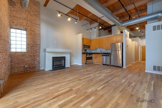 unfurnished living room featuring visible vents, brick wall, baseboards, and a high ceiling