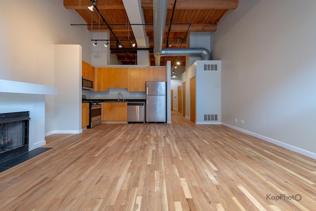 kitchen with a towering ceiling, stainless steel appliances, dark countertops, visible vents, and a sink