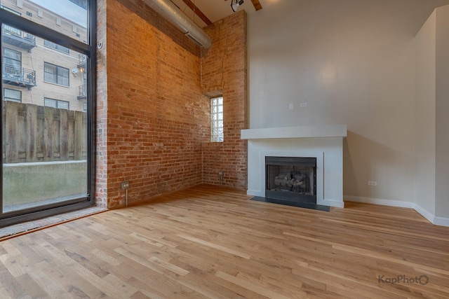 unfurnished living room with a fireplace with flush hearth, brick wall, a high ceiling, and wood finished floors