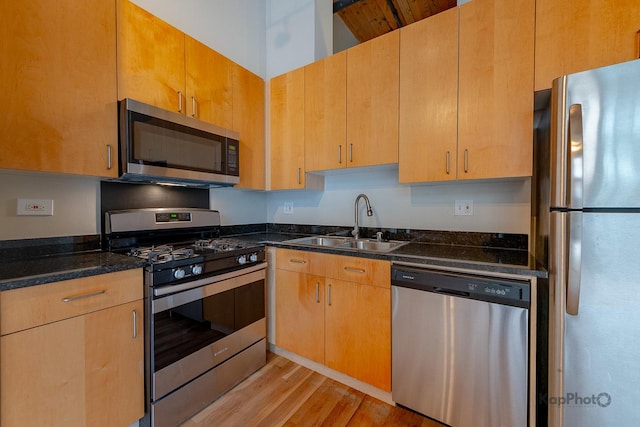kitchen featuring stainless steel appliances, light wood-style flooring, a sink, and dark stone countertops