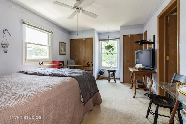 bedroom with light colored carpet, two closets, and a ceiling fan
