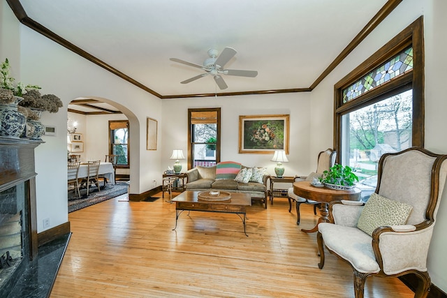 living area featuring light wood-style floors, arched walkways, ornamental molding, and ceiling fan