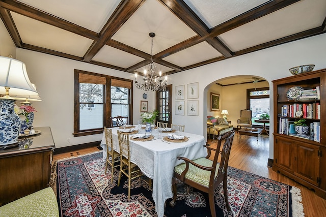 dining area with arched walkways, coffered ceiling, wood finished floors, and a notable chandelier