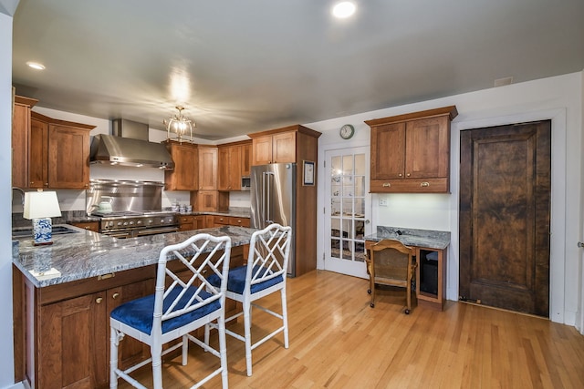 kitchen featuring appliances with stainless steel finishes, a sink, light wood finished floors, wall chimney exhaust hood, and a peninsula