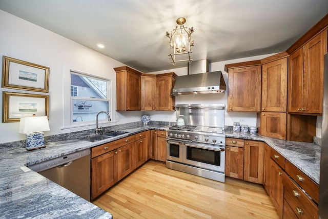 kitchen featuring appliances with stainless steel finishes, brown cabinets, a sink, dark stone countertops, and wall chimney exhaust hood