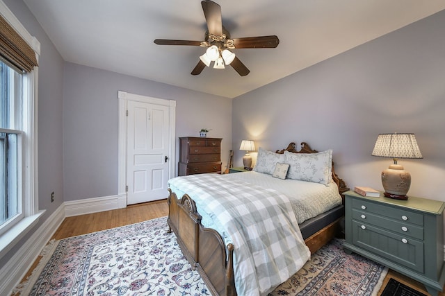 bedroom featuring a ceiling fan, baseboards, multiple windows, and wood finished floors