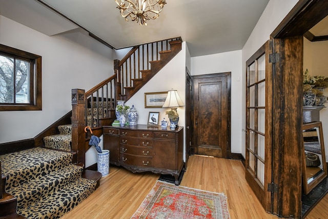 stairway featuring baseboards, wood finished floors, a chandelier, and a healthy amount of sunlight