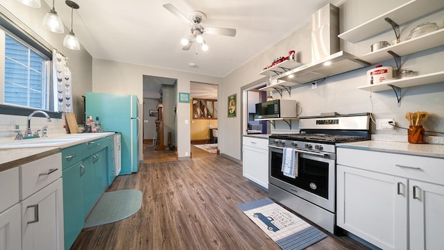 kitchen with stainless steel appliances, dark wood-style floors, a sink, a ceiling fan, and wall chimney range hood