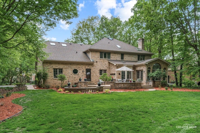 back of property featuring a lawn, brick siding, a chimney, a deck, and a shingled roof