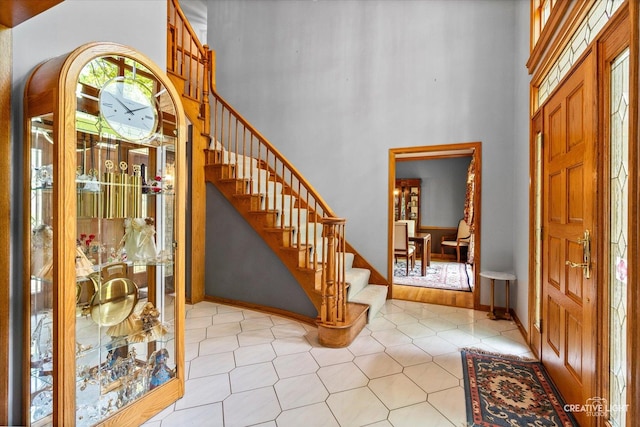 foyer with stairway, a high ceiling, light tile patterned floors, and baseboards