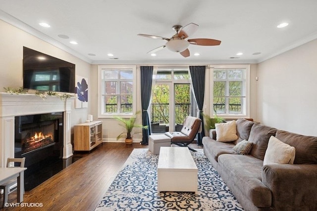 living area with recessed lighting, ornamental molding, dark wood finished floors, ceiling fan, and a fireplace with flush hearth