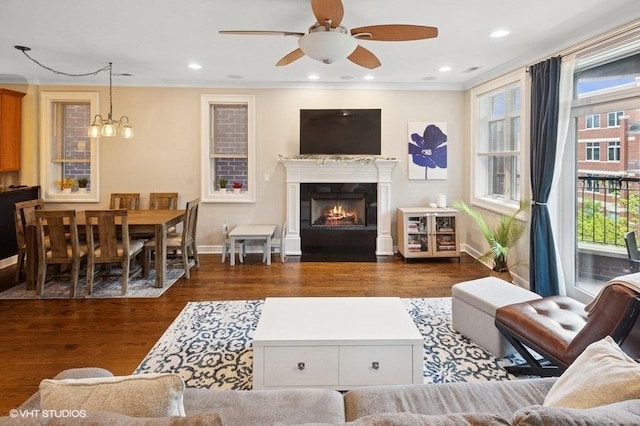 living area featuring ceiling fan with notable chandelier, a fireplace with flush hearth, baseboards, and wood finished floors
