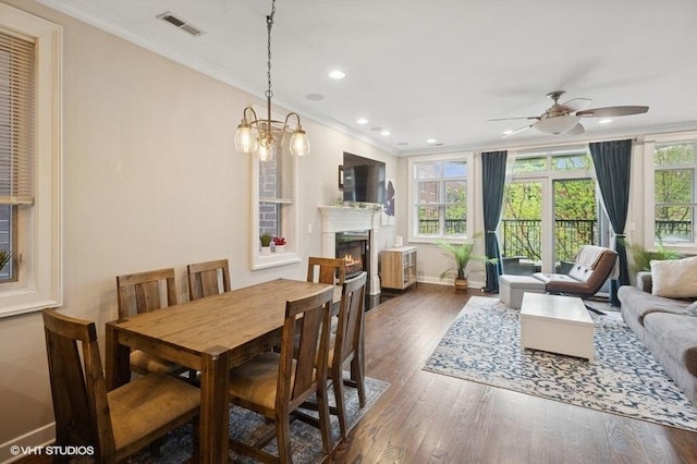 dining space featuring wood finished floors, crown molding, baseboards, ceiling fan, and a warm lit fireplace