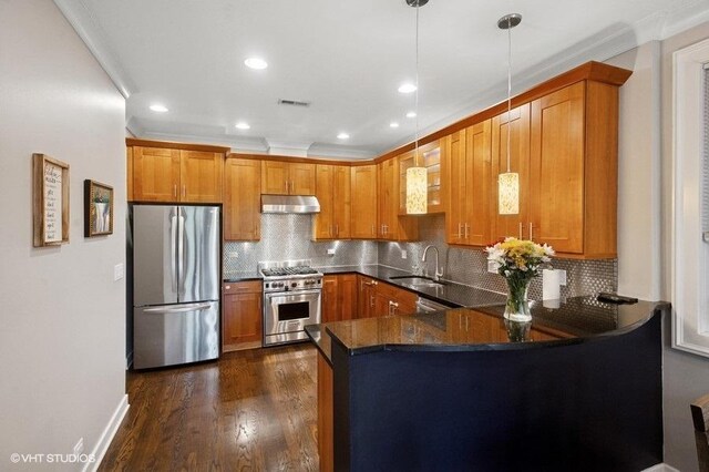 kitchen featuring a sink, a peninsula, brown cabinets, under cabinet range hood, and appliances with stainless steel finishes
