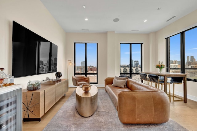 living area with recessed lighting, a city view, visible vents, baseboards, and light wood-style flooring