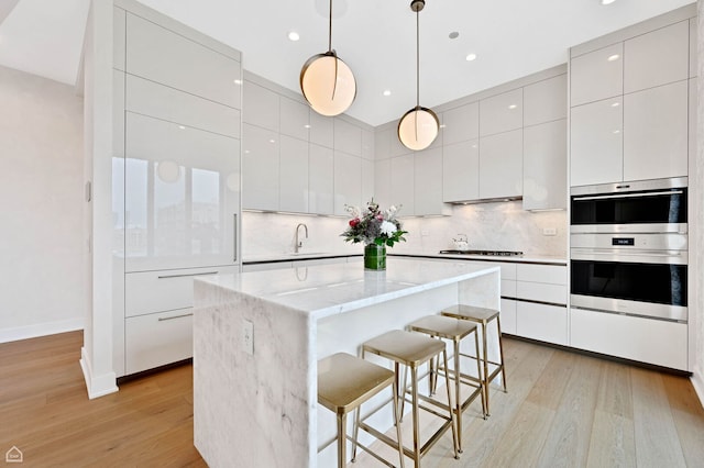 kitchen with a center island, a kitchen breakfast bar, a sink, light wood-style flooring, and modern cabinets