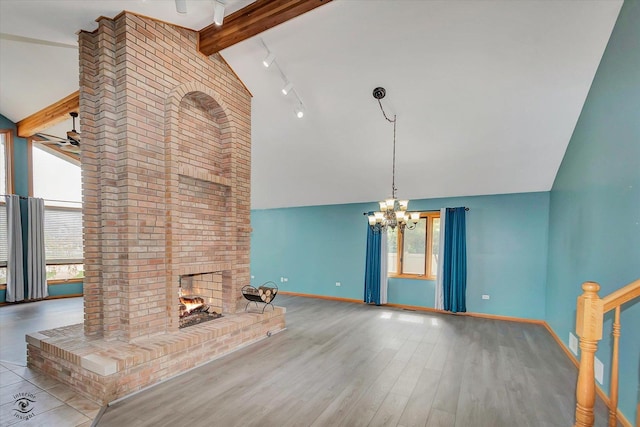 unfurnished living room with a fireplace, rail lighting, high vaulted ceiling, ceiling fan with notable chandelier, and baseboards